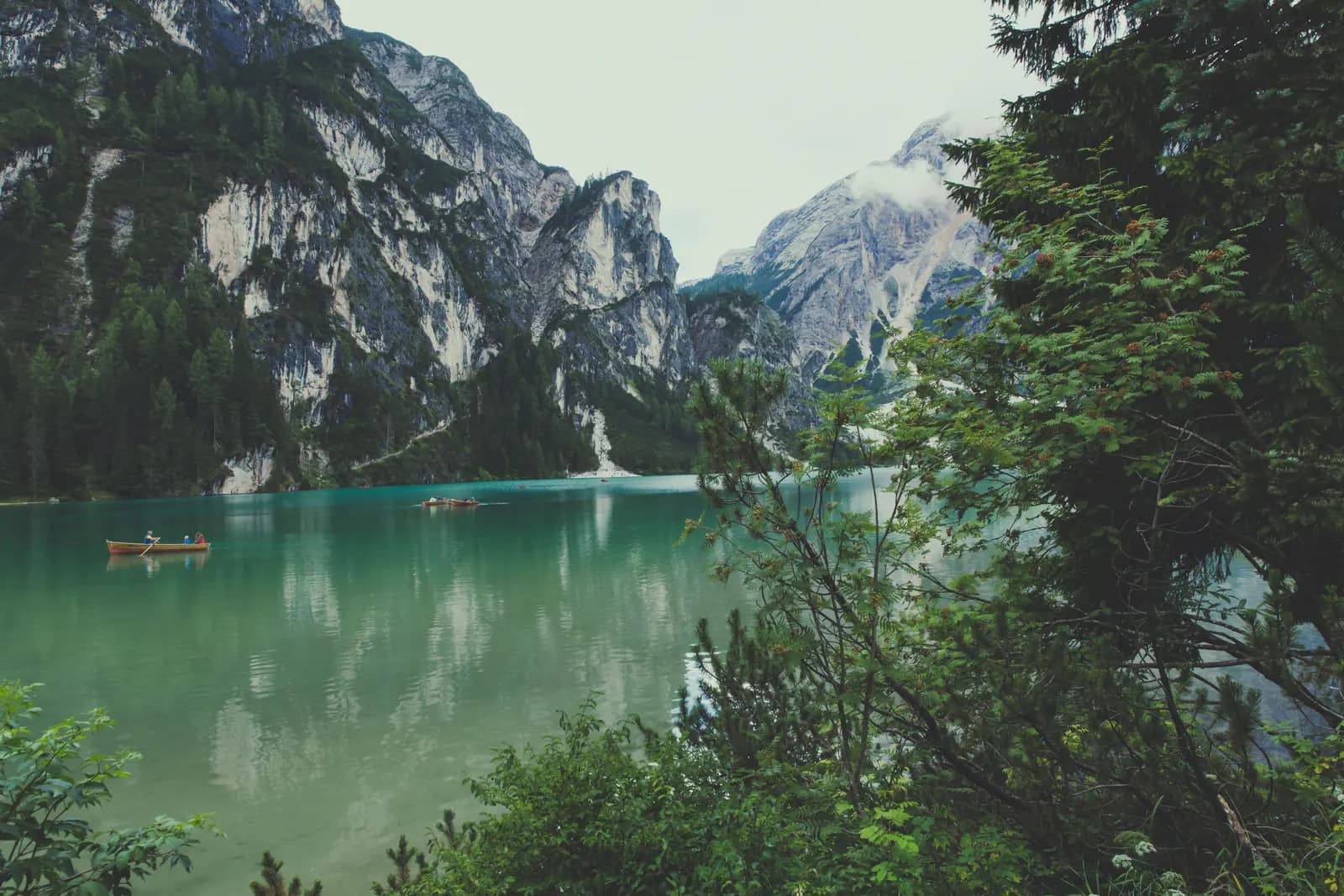 Boats on an alpine lake beneath wooded slopes and mountains