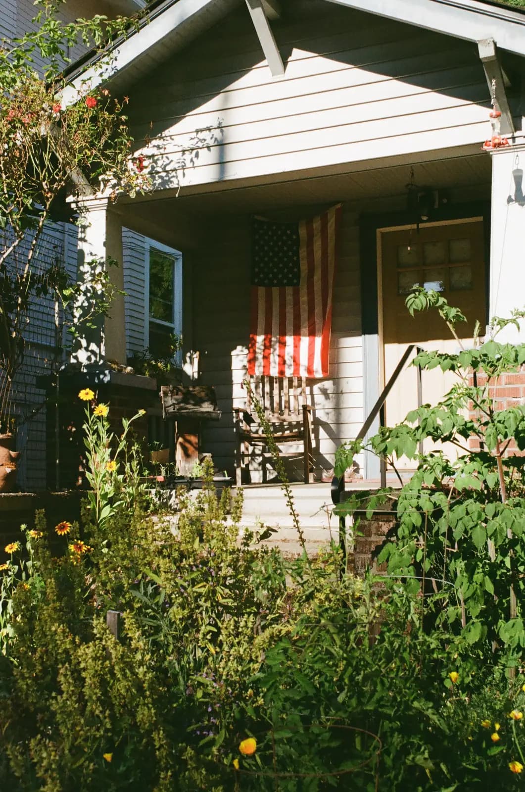 A sunlit front porch with flowers and a garden beyond